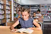 Ung jente leser i en bok i et skolebibliotek.